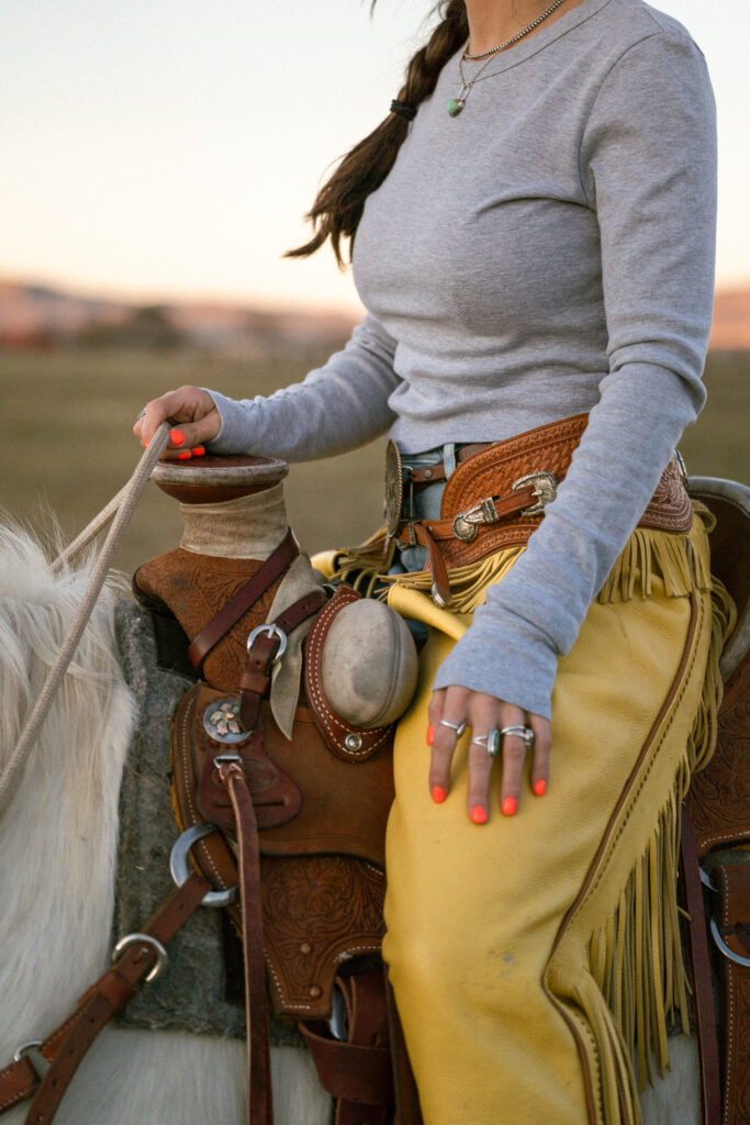 Close-up of a woman in yellow leather chaps holding reins on horseback, showcasing Western lifestyle fashion and outdoor brand photography by Josi Frommelt.